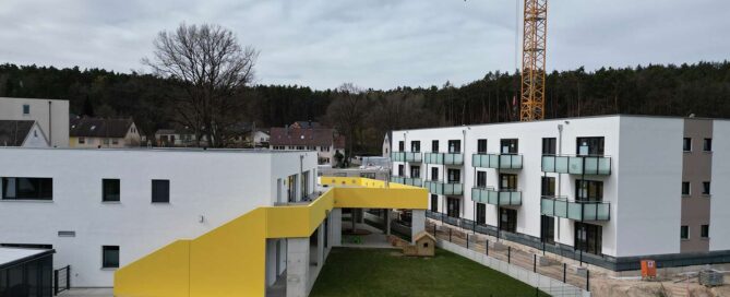 Luftaufnahme von Kita in Wolkersdorf. Daneben steht eine moderne Wohnanlage mit Flachdach.